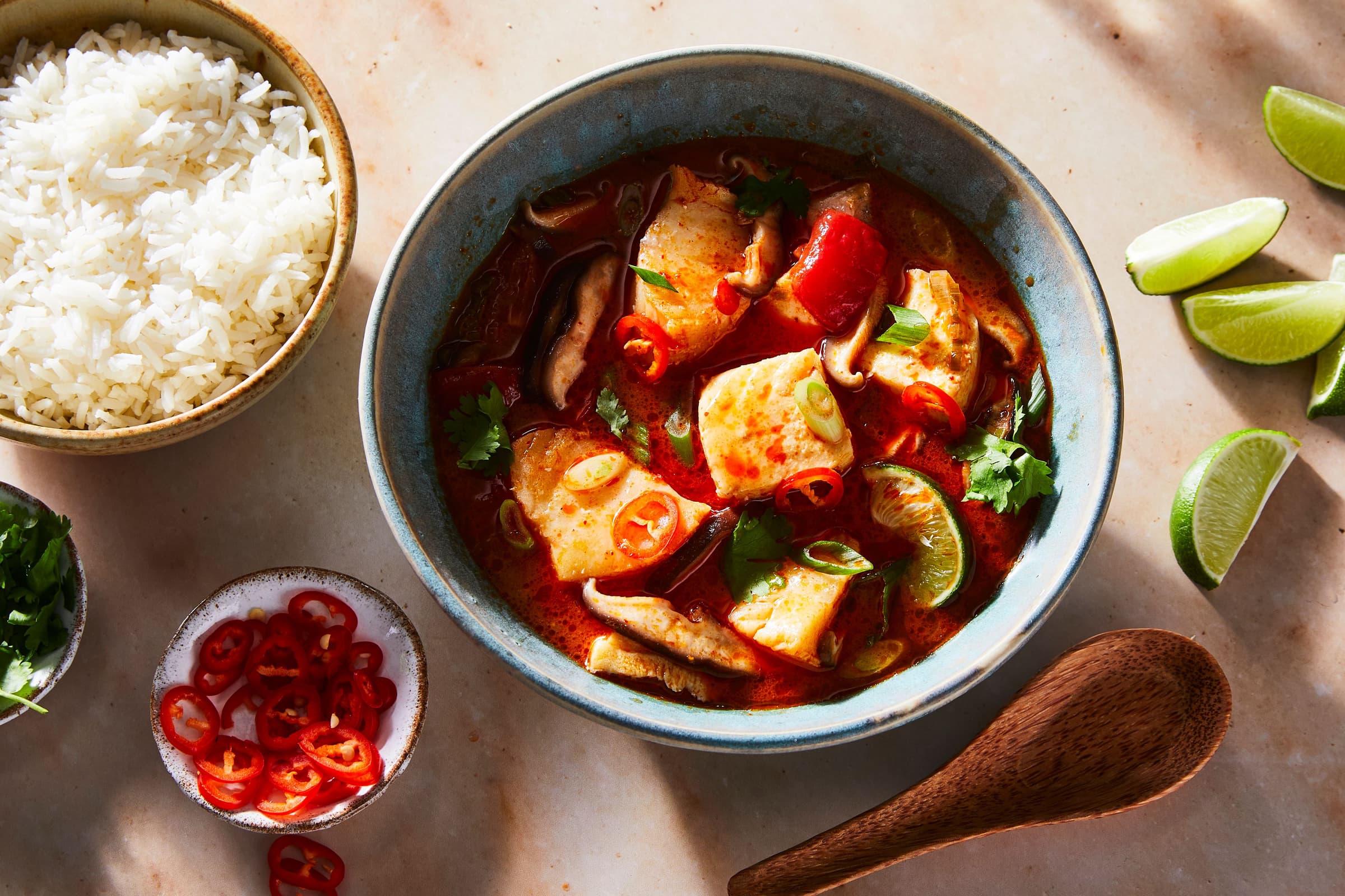 bowl of seafood soup with bowls of rice, chiles, and herbs
