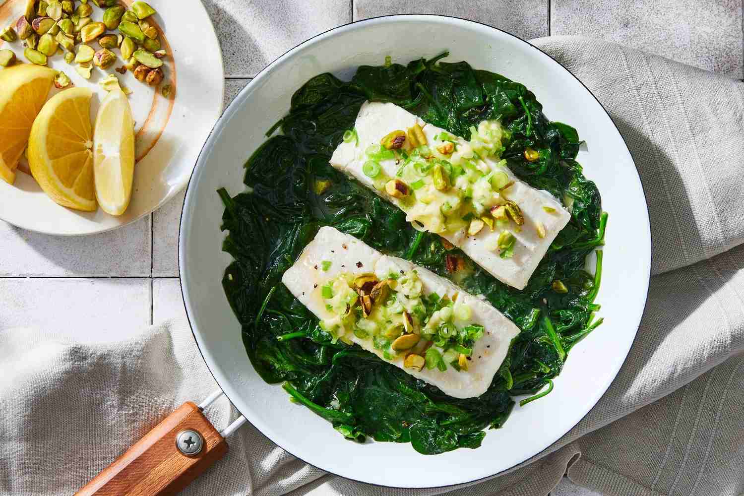 halibut and spinach in a skillet with lemon wedges and pistachios