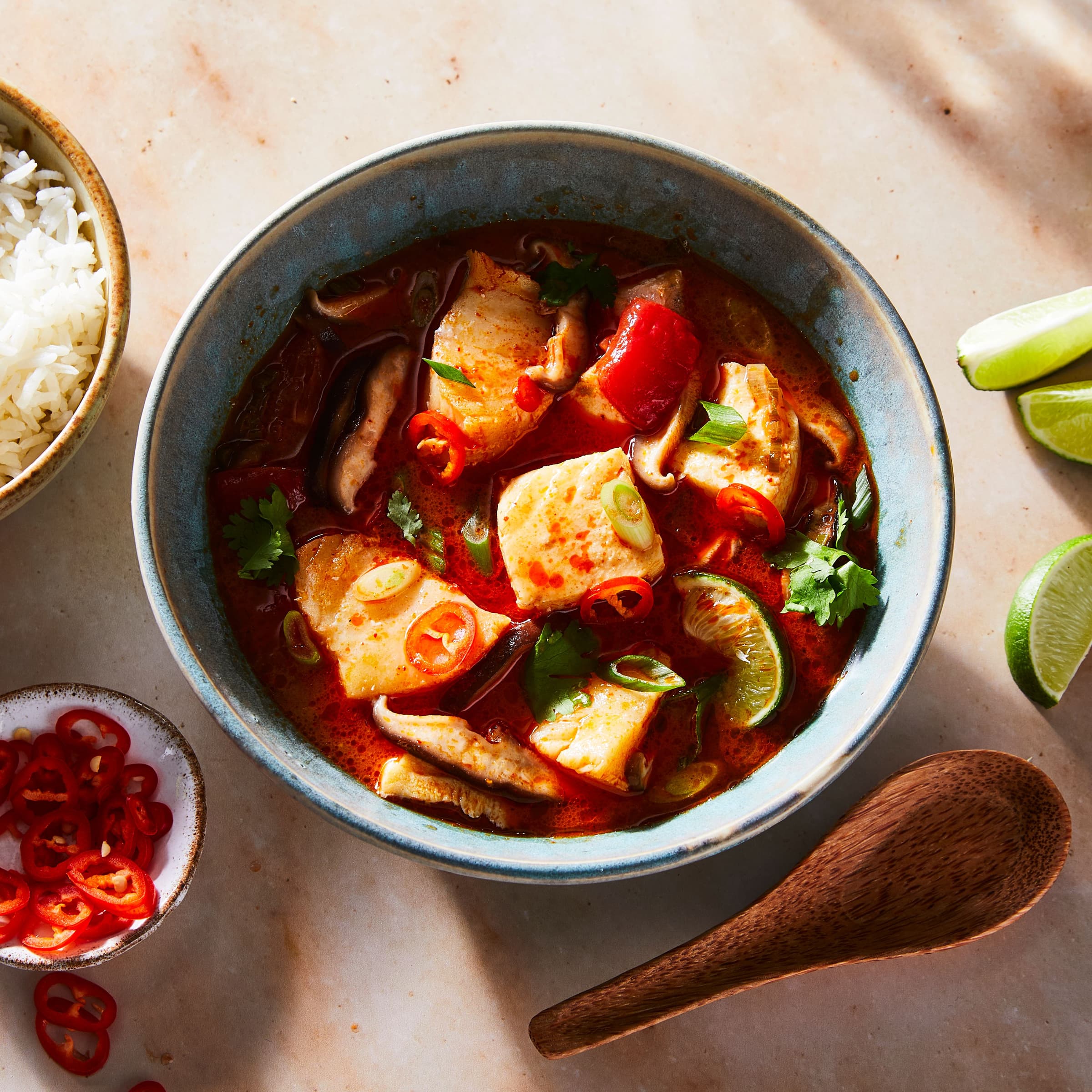 bowl of seafood soup with bowls of rice, chiles, and herbs