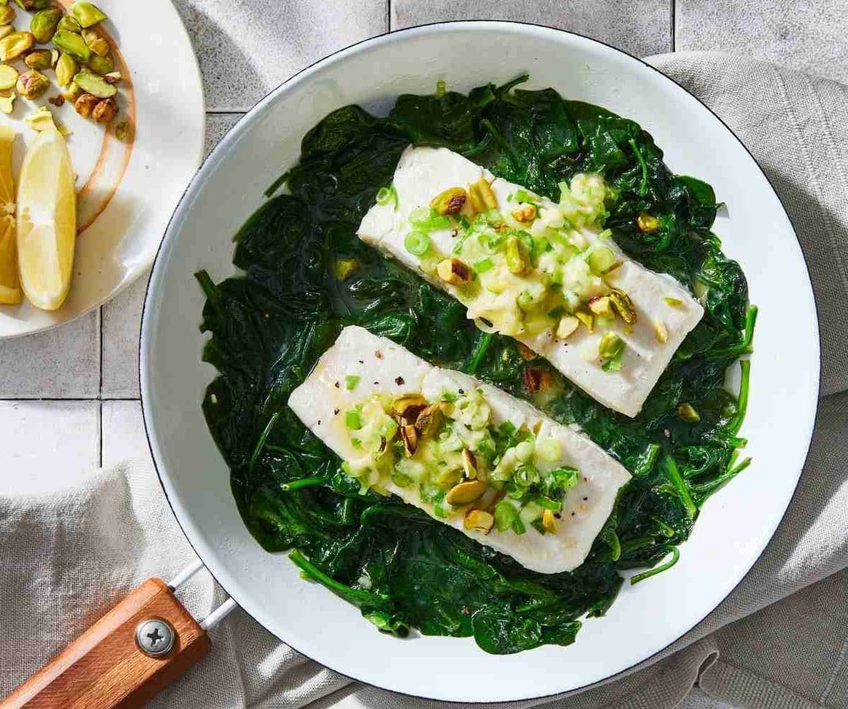 halibut and spinach in a skillet with lemon wedges and pistachios