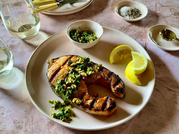 salmon steak on a plate with herb sauce and lemon wedges