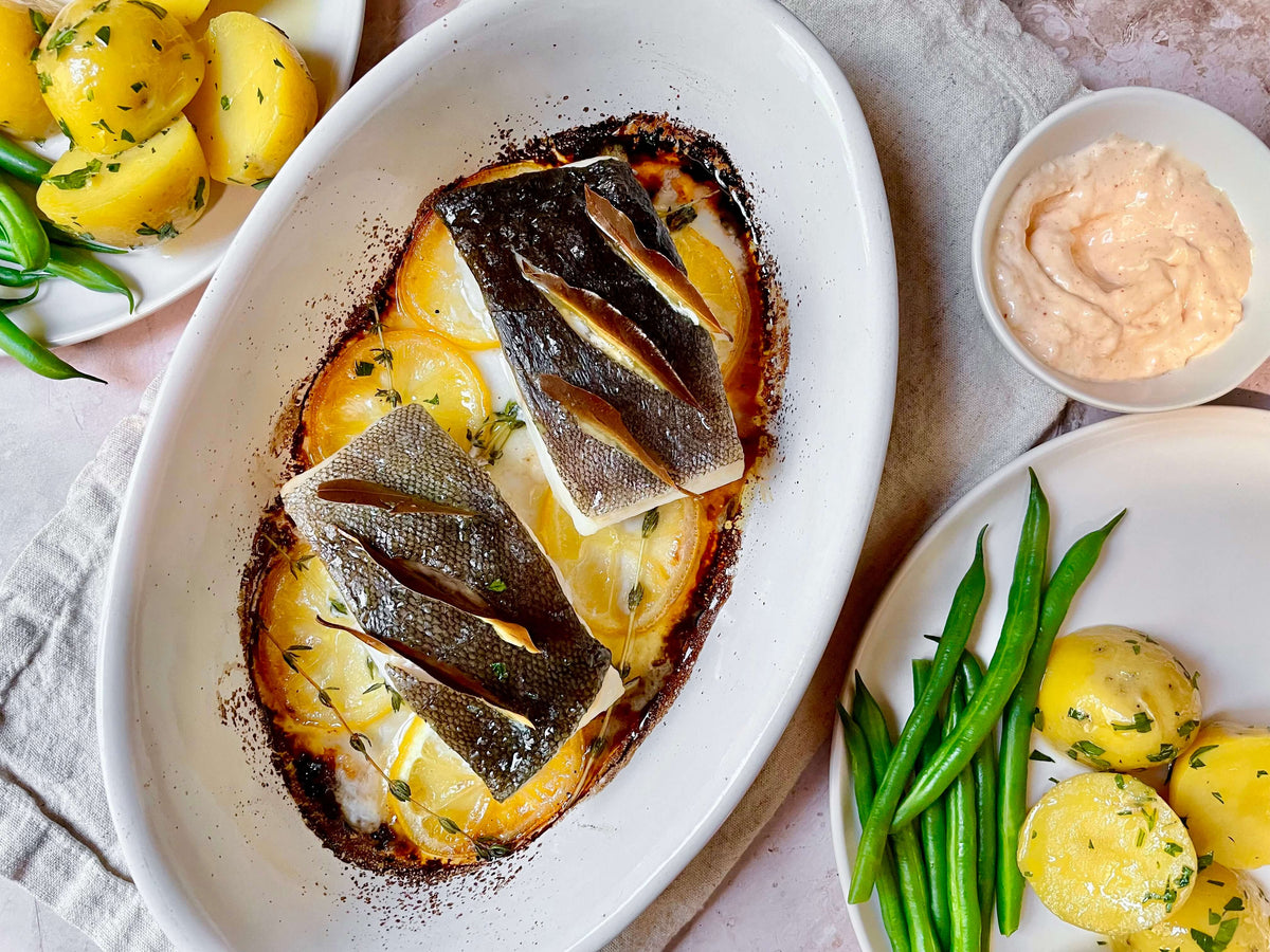 fish in a baking dish with plates of potatoes and beans on the side