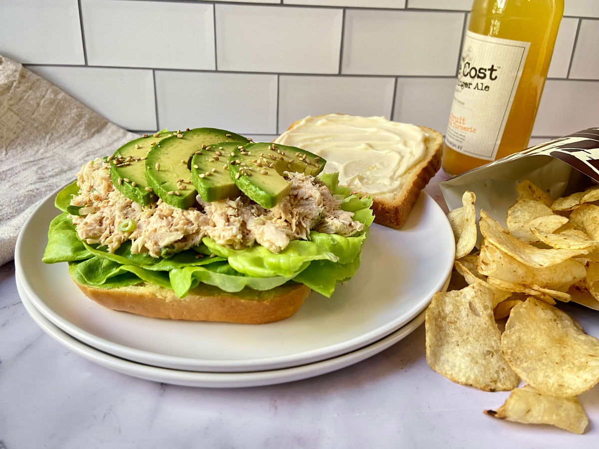 a tuna sandwich with avocado on a plate and potato chips on the side