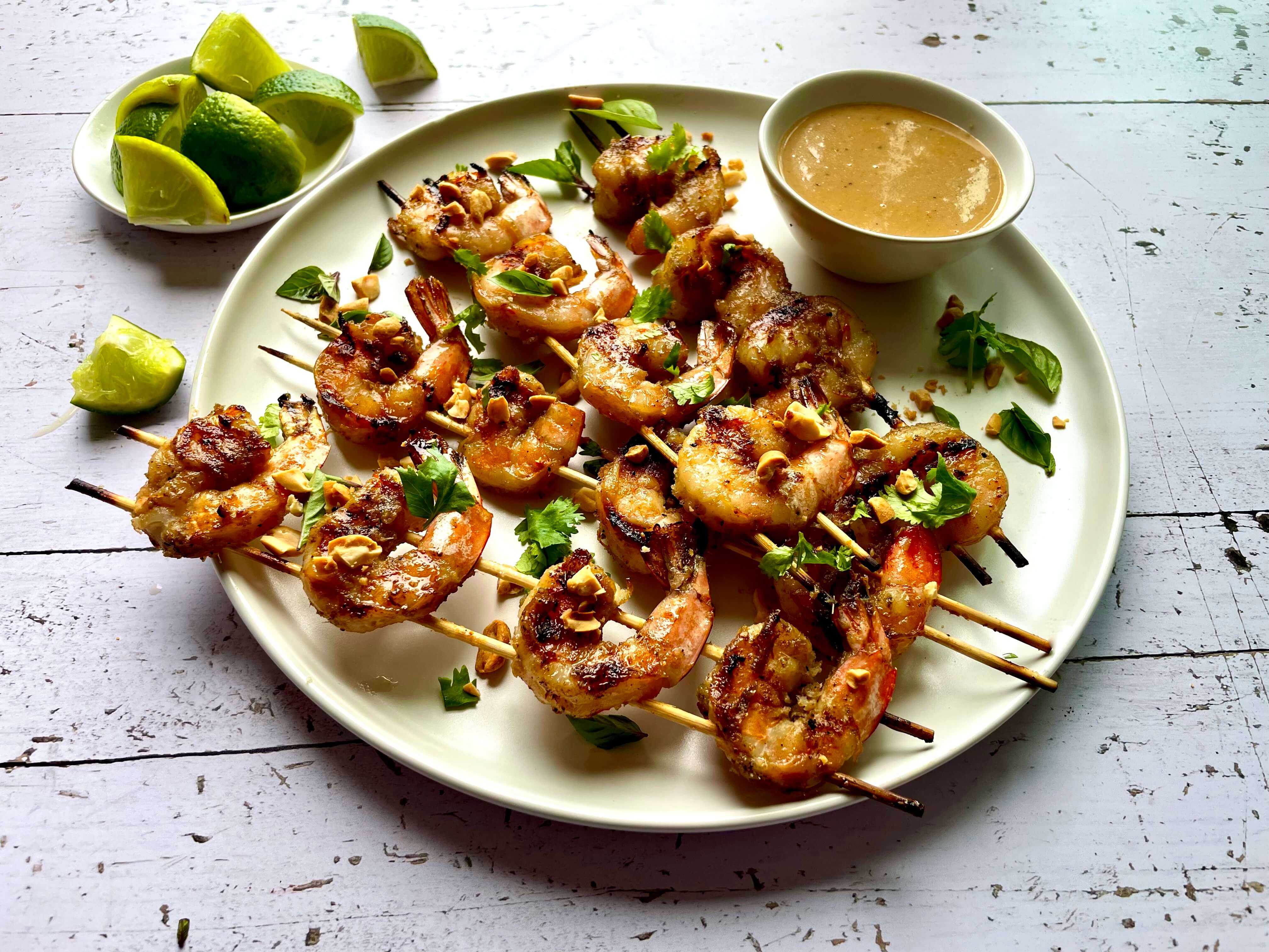 plate of shrimp skewers with a bowl of sauce and lime wedges