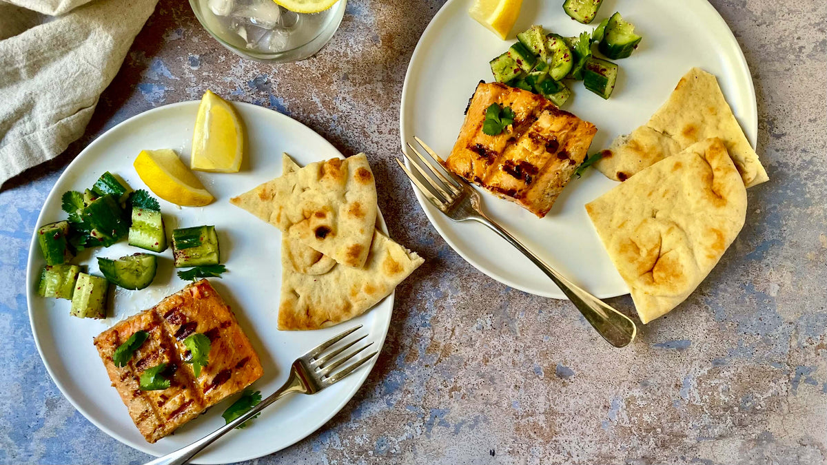 2 plates with salmon, lemons, cucumbers and naan